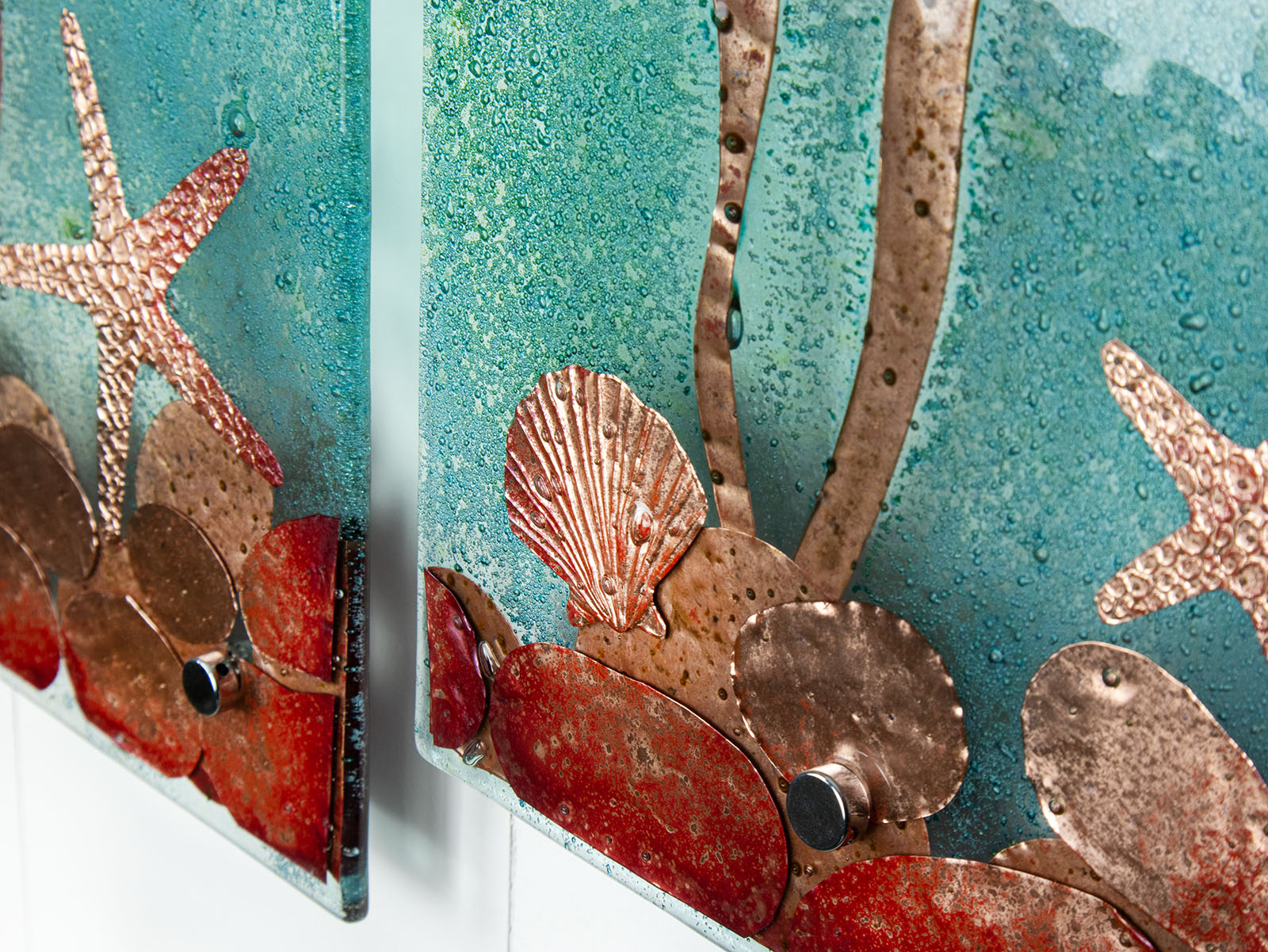 Seashell copper details on a fused glass staggered triptych, with hand-etched copper seahorses and ocean flora and an ocean blue background. 