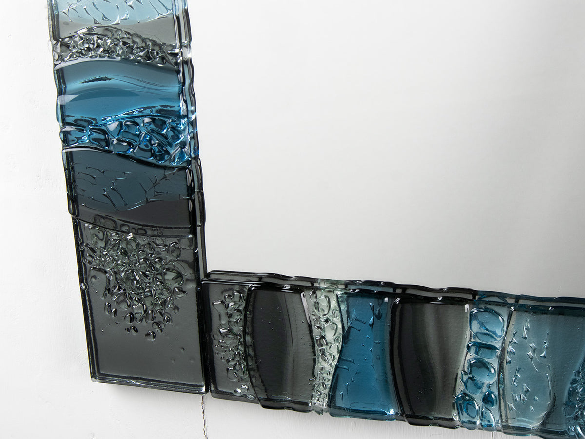 Details on a fused glass oblong mirror, handmade using soft coastal blue tinted and grey glass with delicate texture and a wavy design.