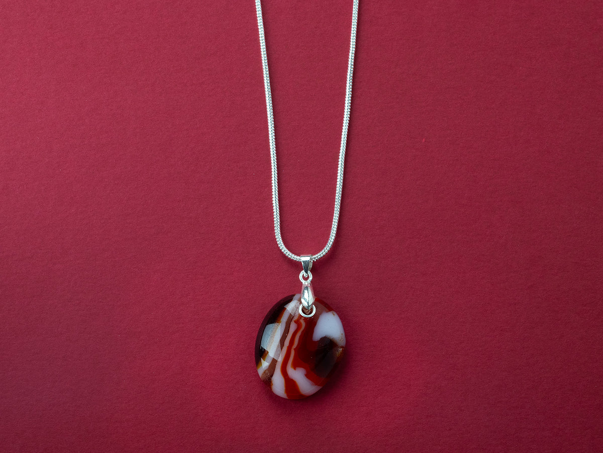 A sterling silver chain necklace with a round fused glass pendant featuring an autumnal, red design, handmade in vibrant colours. 