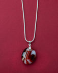 A sterling silver chain necklace with a round fused glass pendant featuring an autumnal, red design, handmade in vibrant colours. 