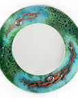 A circular fused glass round mirror, handmade in vibrant aquas and sea greens, with darting copper fish. 