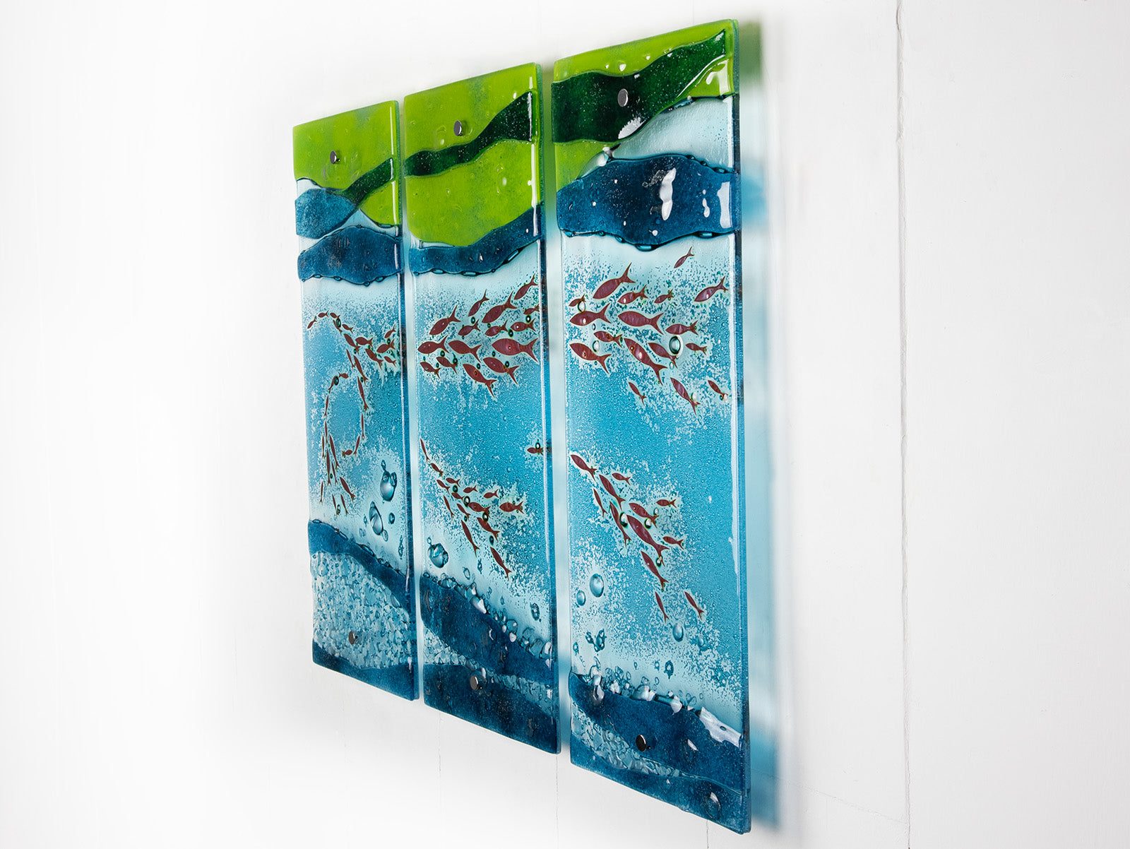 A side view of a fused glass triptych featuring marine blues and greens in an ocean design, with copper fish and textured detail. 