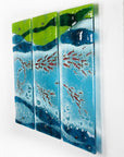 A side view of a fused glass triptych featuring marine blues and greens in an ocean design, with copper fish and textured detail. 