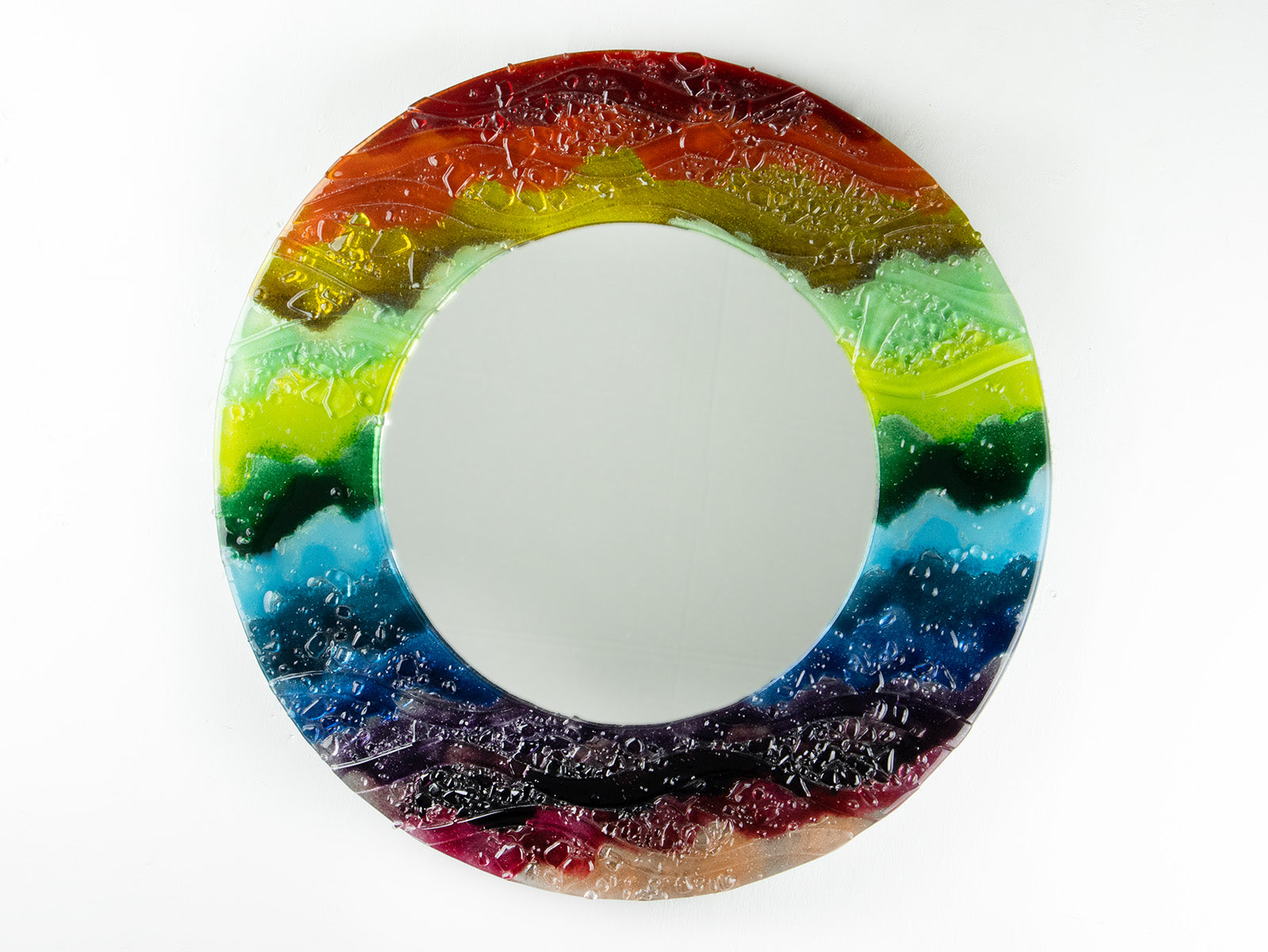A circular fused glass round mirror in a vibrant rainbow colour-way with soft waves and textured detailing. 