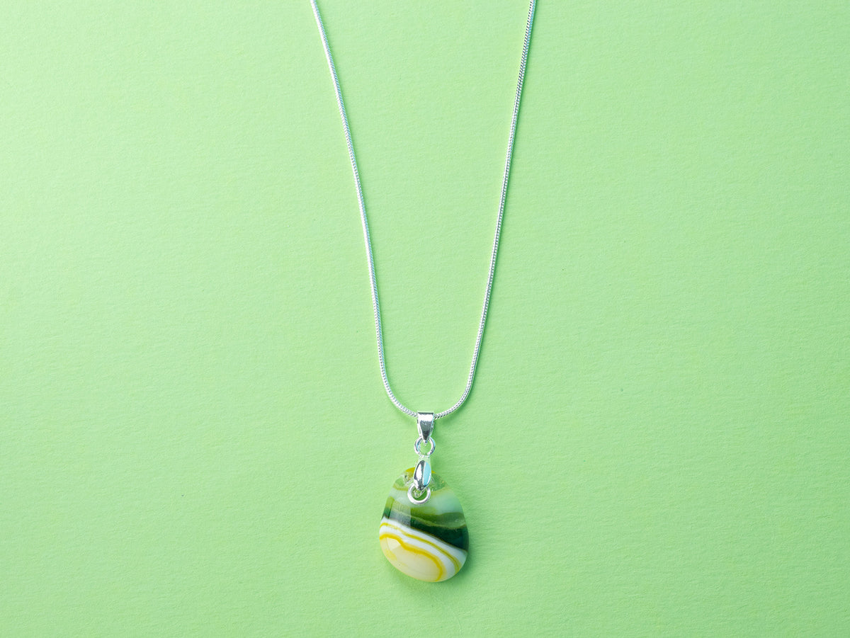 A sterling silver chain necklace with a teardrop-shaped fused glass pendant handmade featuring a golden yellow and sea greens in a marbled design.