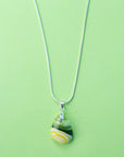A sterling silver chain necklace with a teardrop-shaped fused glass pendant handmade featuring a golden yellow and sea greens in a marbled design.