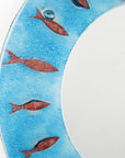 A close up of a fused glass round mirror in an aqua colour-way featuring a circular design of copper fish.