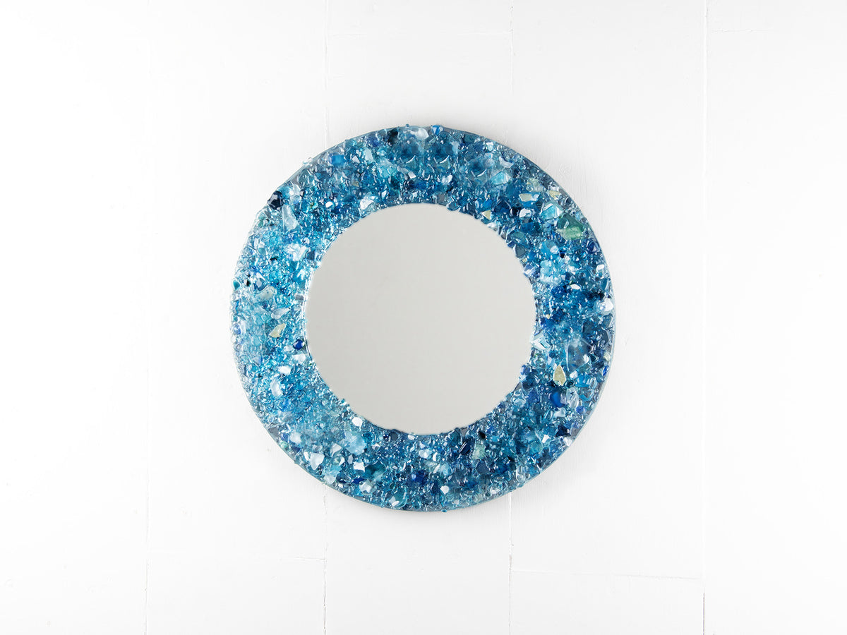 A fused glass round mirror, handmade using recycled crushed glass in ocean blue hues, with lots of organic texture. 