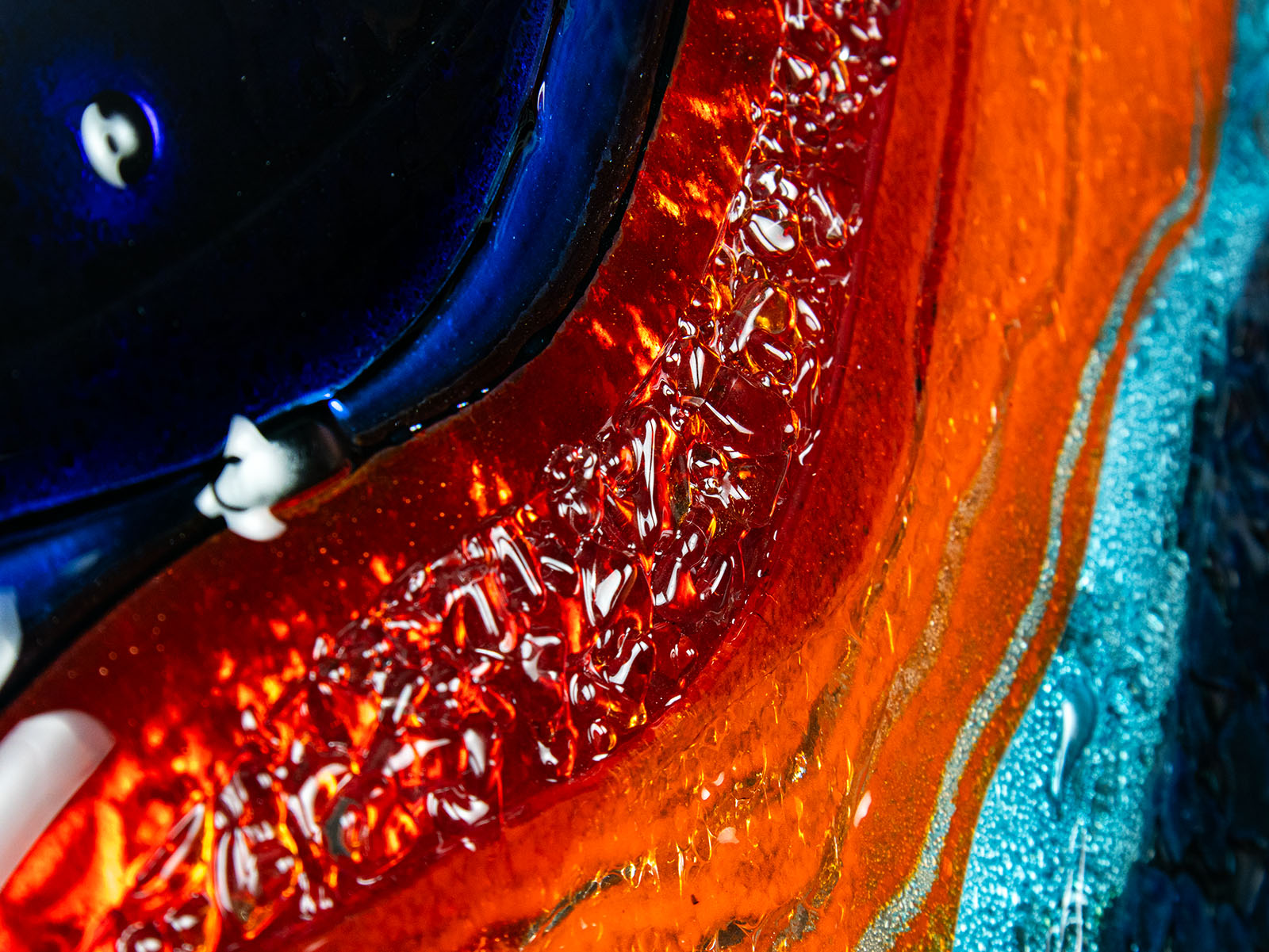 A detailed image of a circular fused glass wall panel featuring abstract wave design in ocean blues and bright oranges, with textured detailing. 