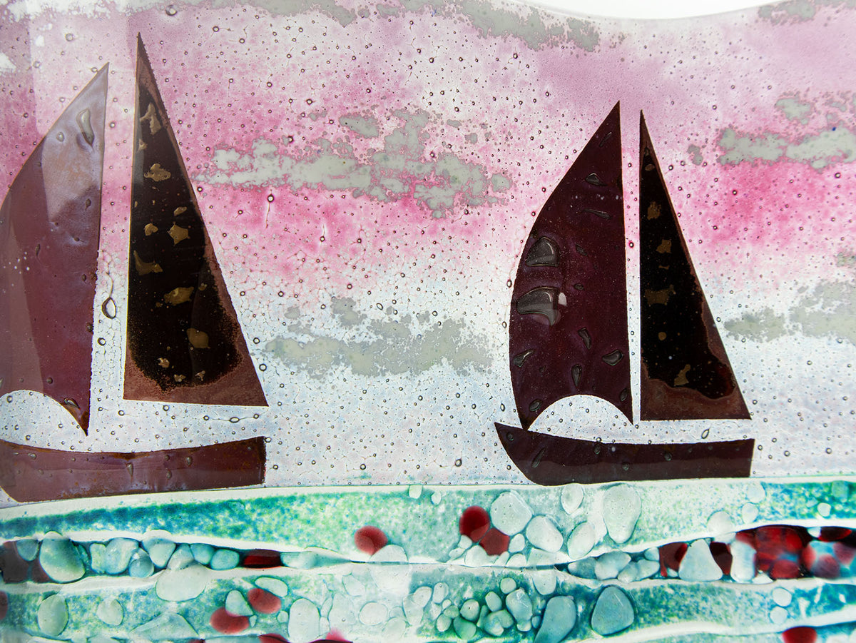 A close up of a fused glass wave panel featuring two metal fish boats and a bright coastal, sunset design with texture. 