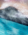 A close up of a circular wall art fused glass panel featuring a scenic landscape with a blue and purple sky, misty mountains, and turquoise water. 