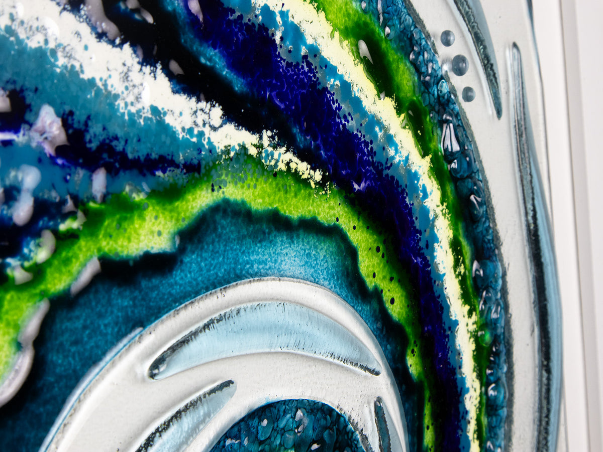 A close up of a fused glass large oblong art frame featuring an abstract tidal design in ocean blue and greens with textural detailing. A handmade coastal inspired piece of wall art. 