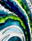 A close up of a fused glass large oblong art frame featuring an abstract tidal design in ocean blue and greens with textural detailing. A handmade coastal inspired piece of wall art. 