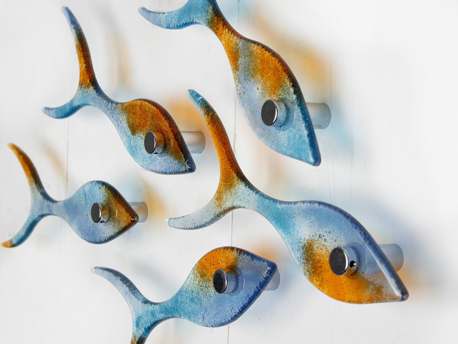 Side image of small display of fused glass fish, individually handmade in sunset orange and sea blue colours. 
