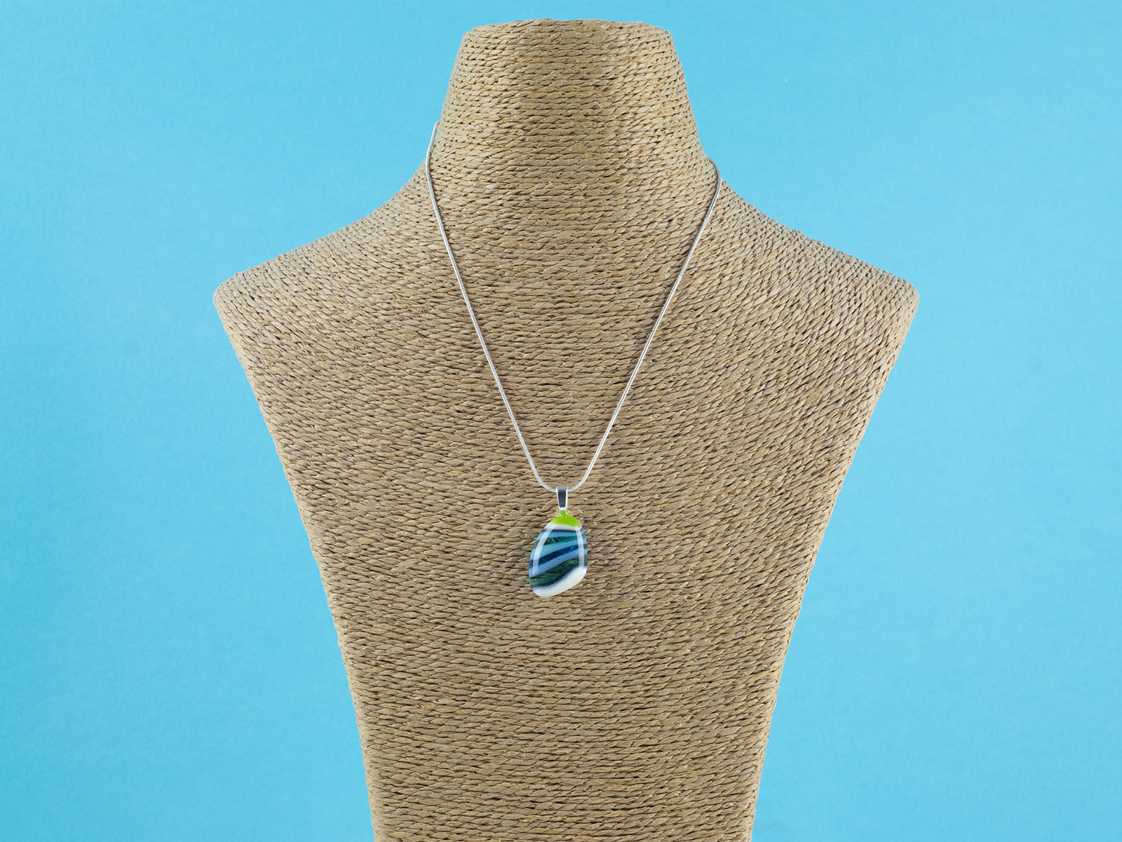 A teardrop-shaped fused glass pendant necklace with a marbled pattern of green, blue, and light teal, suspended on a sterling silver chain.