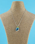 A teardrop-shaped fused glass pendant necklace with a marbled pattern of green, blue, and light teal, suspended on a sterling silver chain.