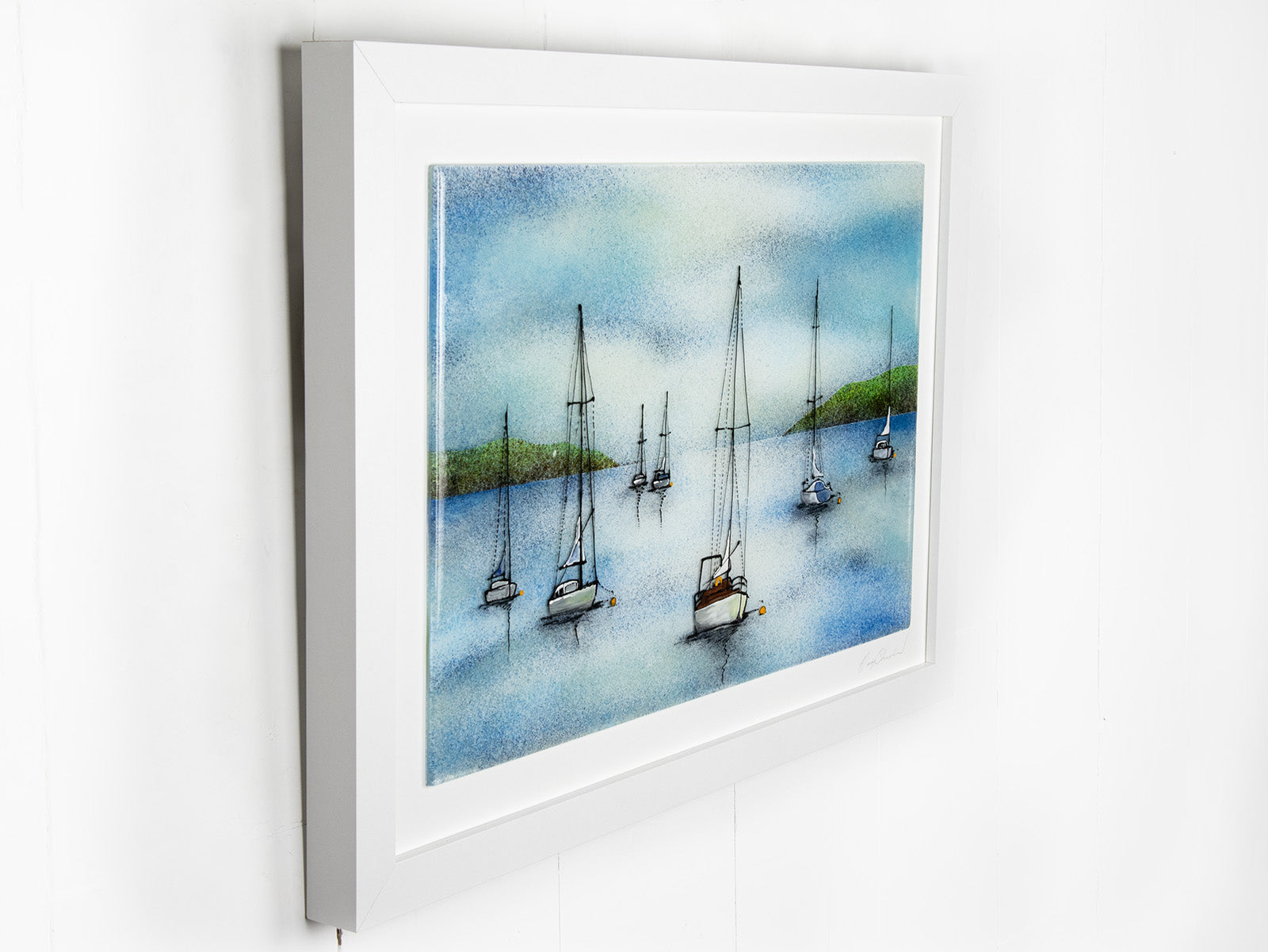 A hand-painted fused glass design of several sailboats anchored, designed in soft coastal colours and presented in a white frame.
