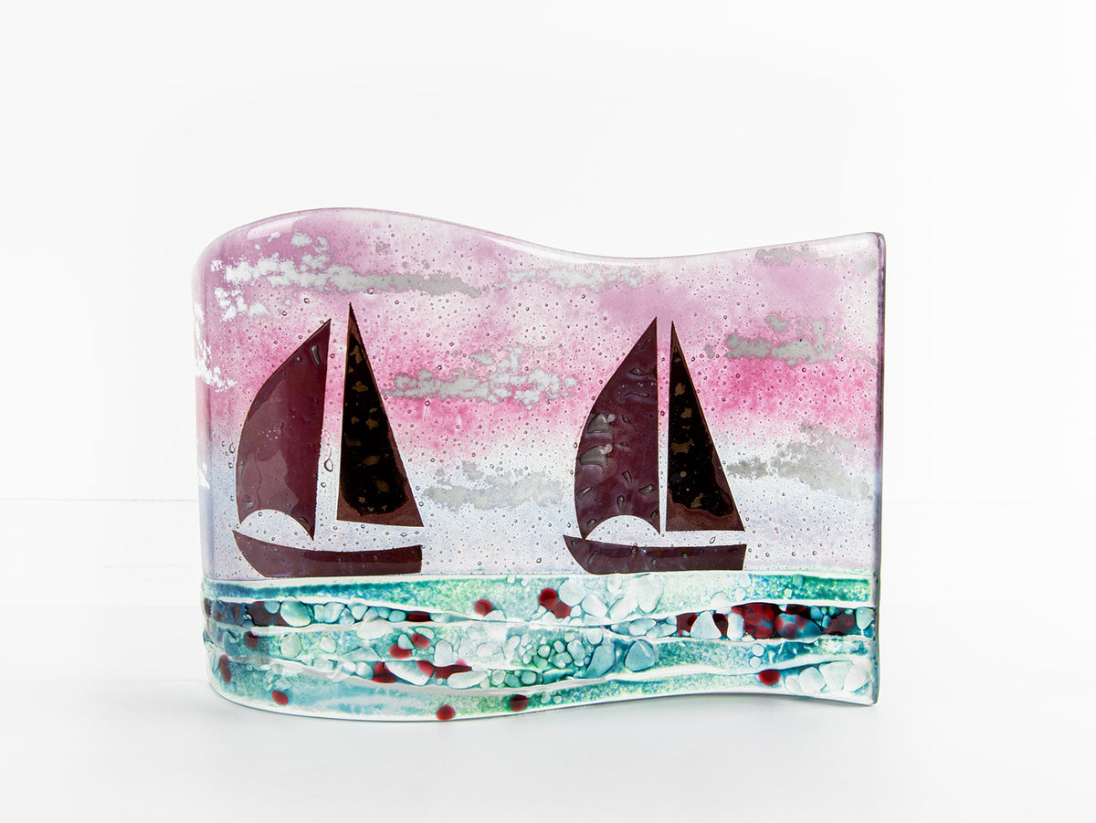 A fused glass wave panel featuring two metal fish boats and a bright coastal, sunset design with texture. 
