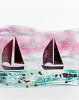 A fused glass wave panel featuring two metal fish boats and a bright coastal, sunset design with texture. 