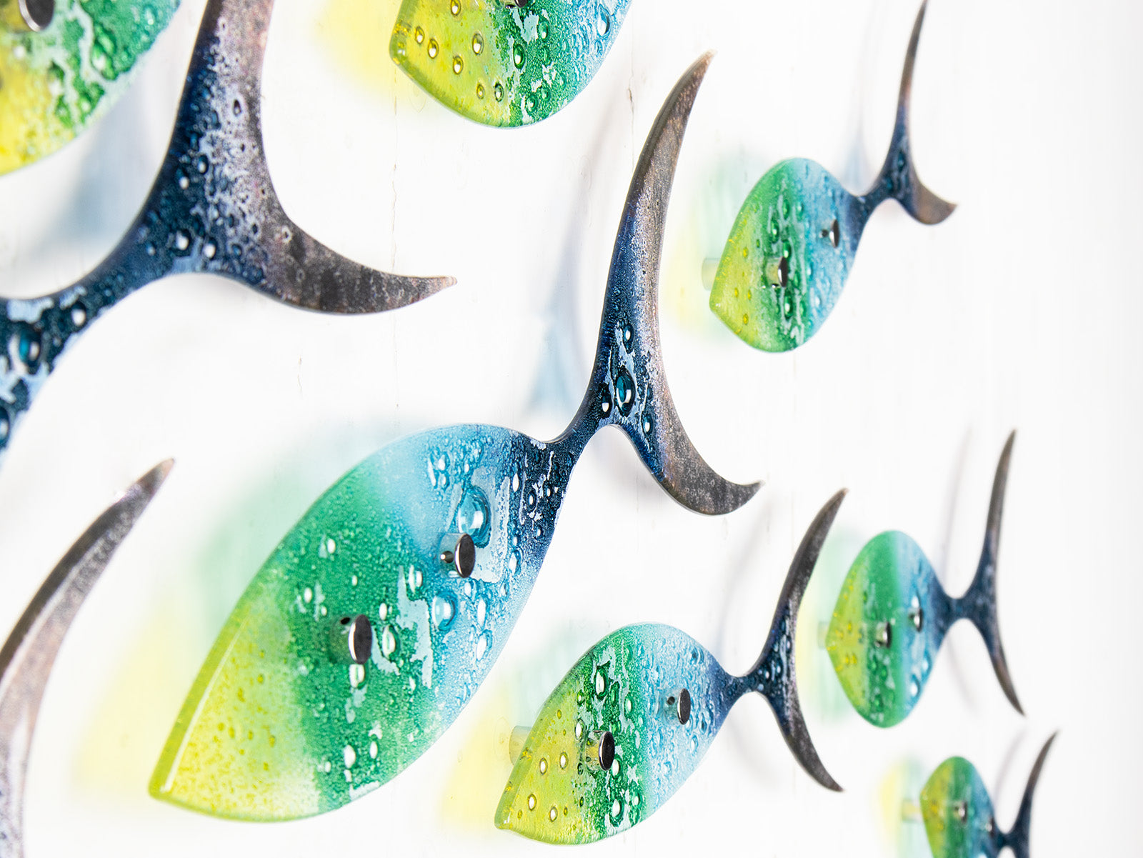 A close up of a fused glass ocean shoal of fish, in bright coastal yellows, purples, greens and blues. A vibrant ocean inspired wall art display. 
