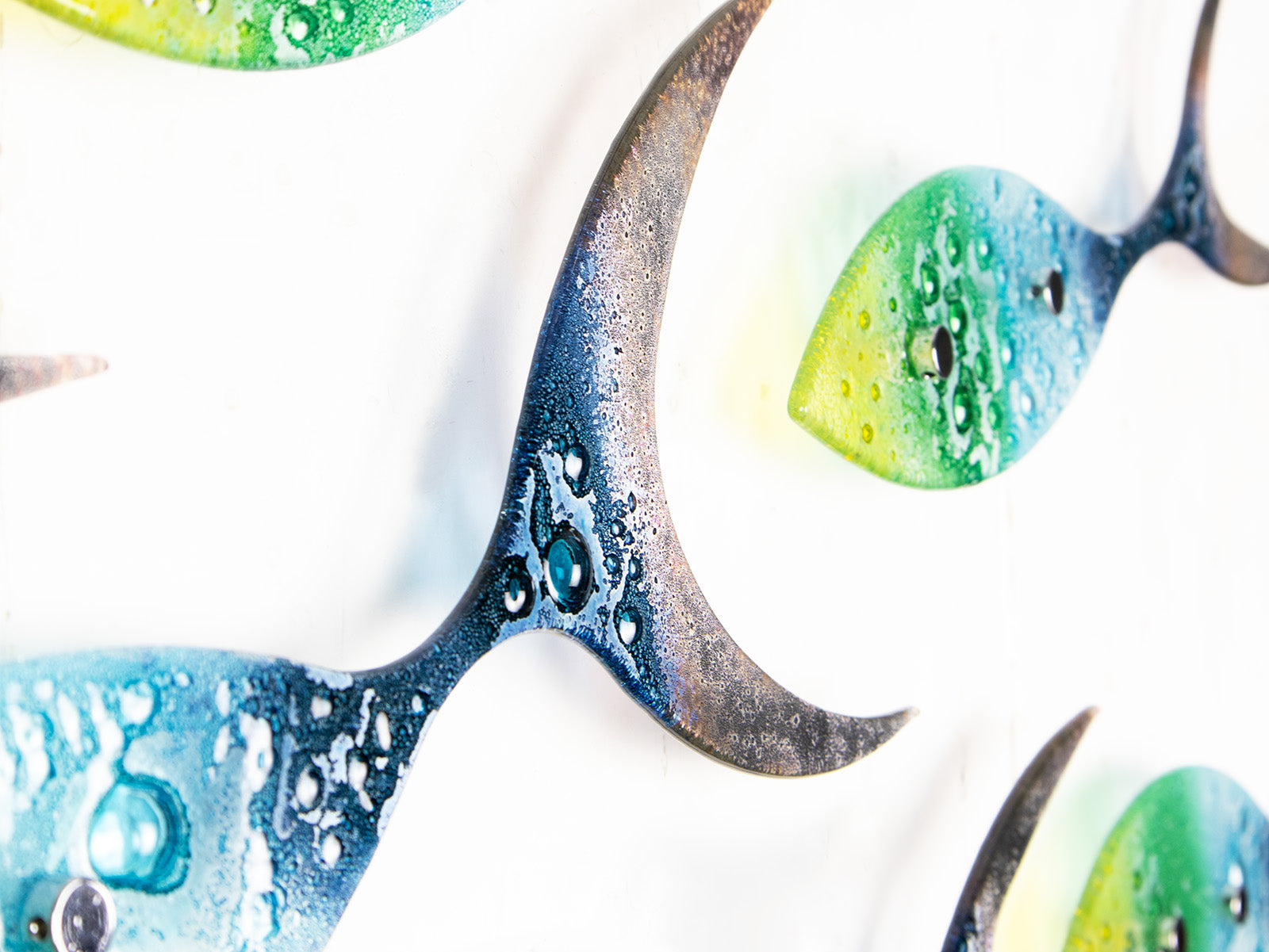 Details of a fused glass ocean shoal of fish, in bright coastal yellows, purples, greens and blues. A vibrant ocean inspired wall art display. 