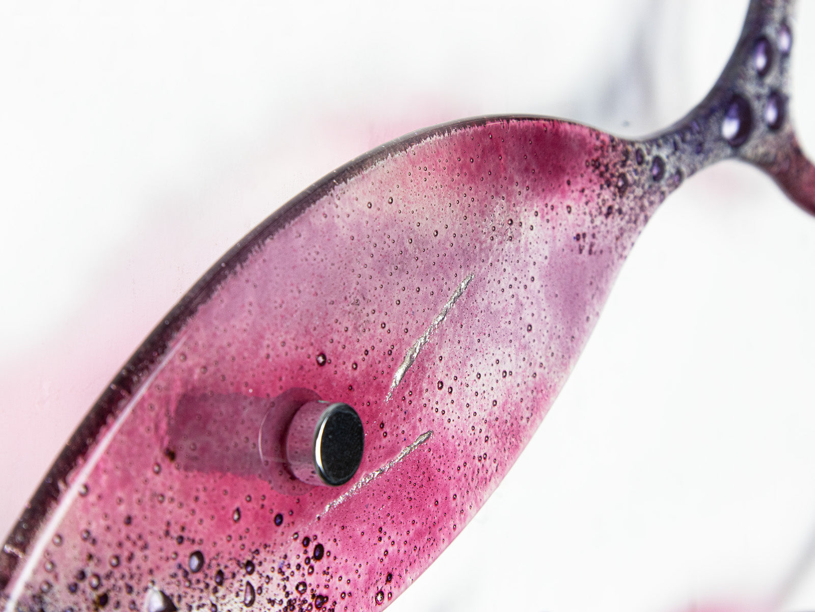 A close up of the shimmering silver detailing on a fused glass shoal of fish, with individual fish installed in a bright pink and bubbled purple colour-way. 