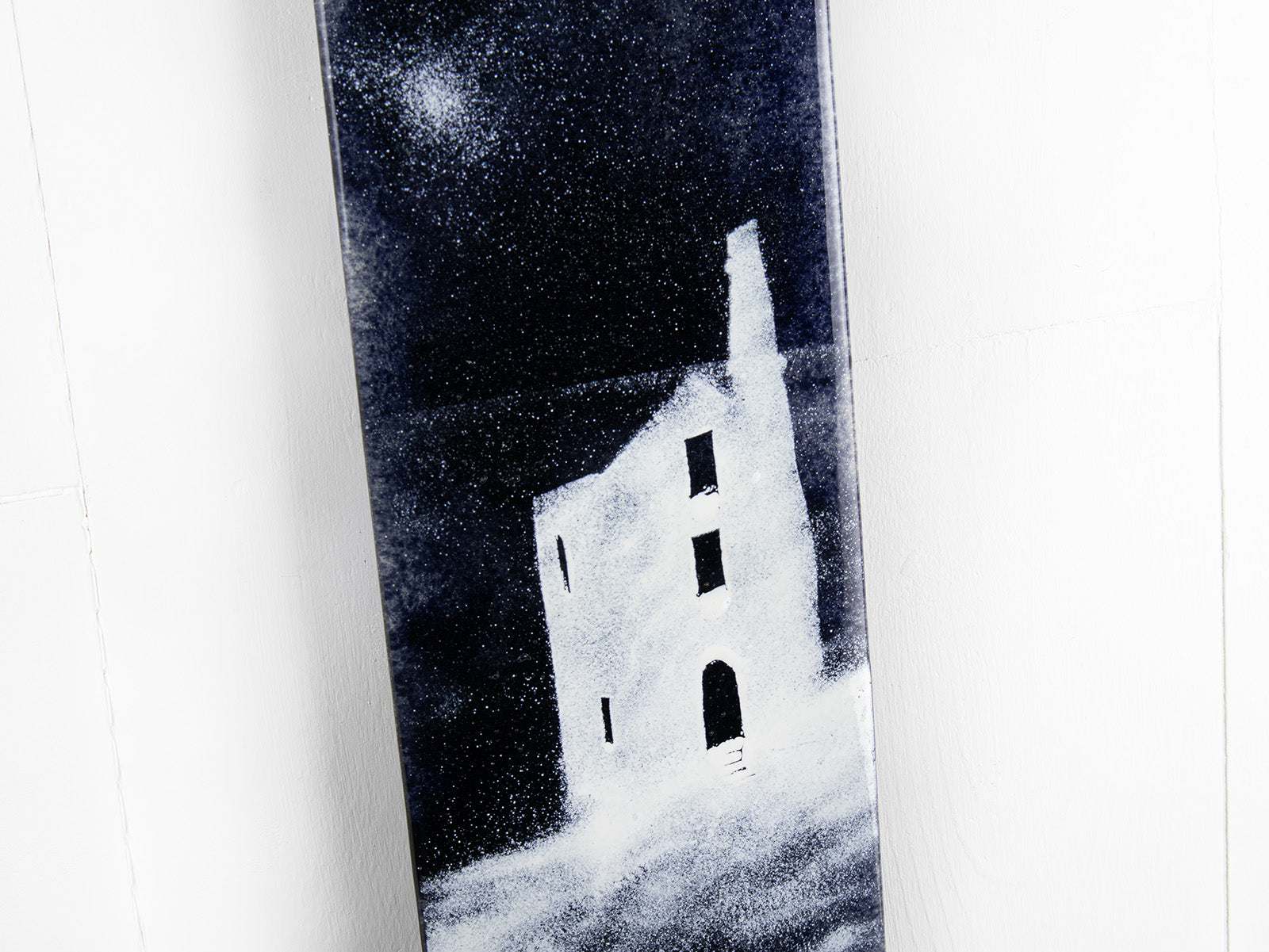 A close up of a fused glass panel featuring a monochrome design of a Cornish tin min. 