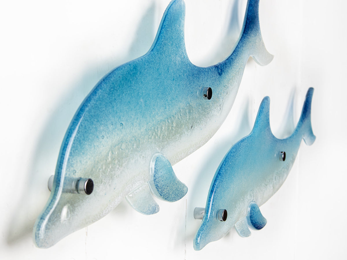 Two blue dolphin wall art panels, handmade i fused glass, designed in soft coastal blues and whites. 