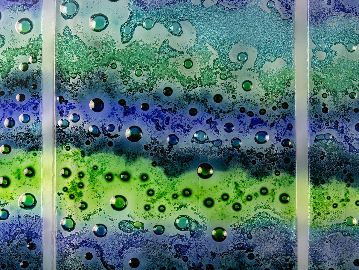 A close up of the details designed on a fused glass staggered triptych featuring an ocean inspired design, with a blend of coastal blues and sea greens, handmade with organic bubbled texture. 