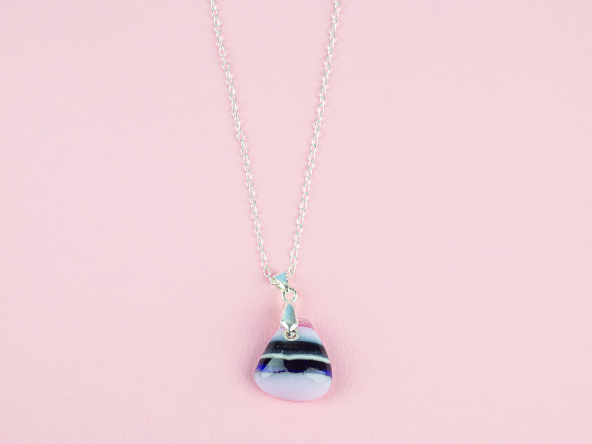 A fused glass pendant necklace, handmade in rose pinks, with dark blues hues, hung on a sterling silver chain.  