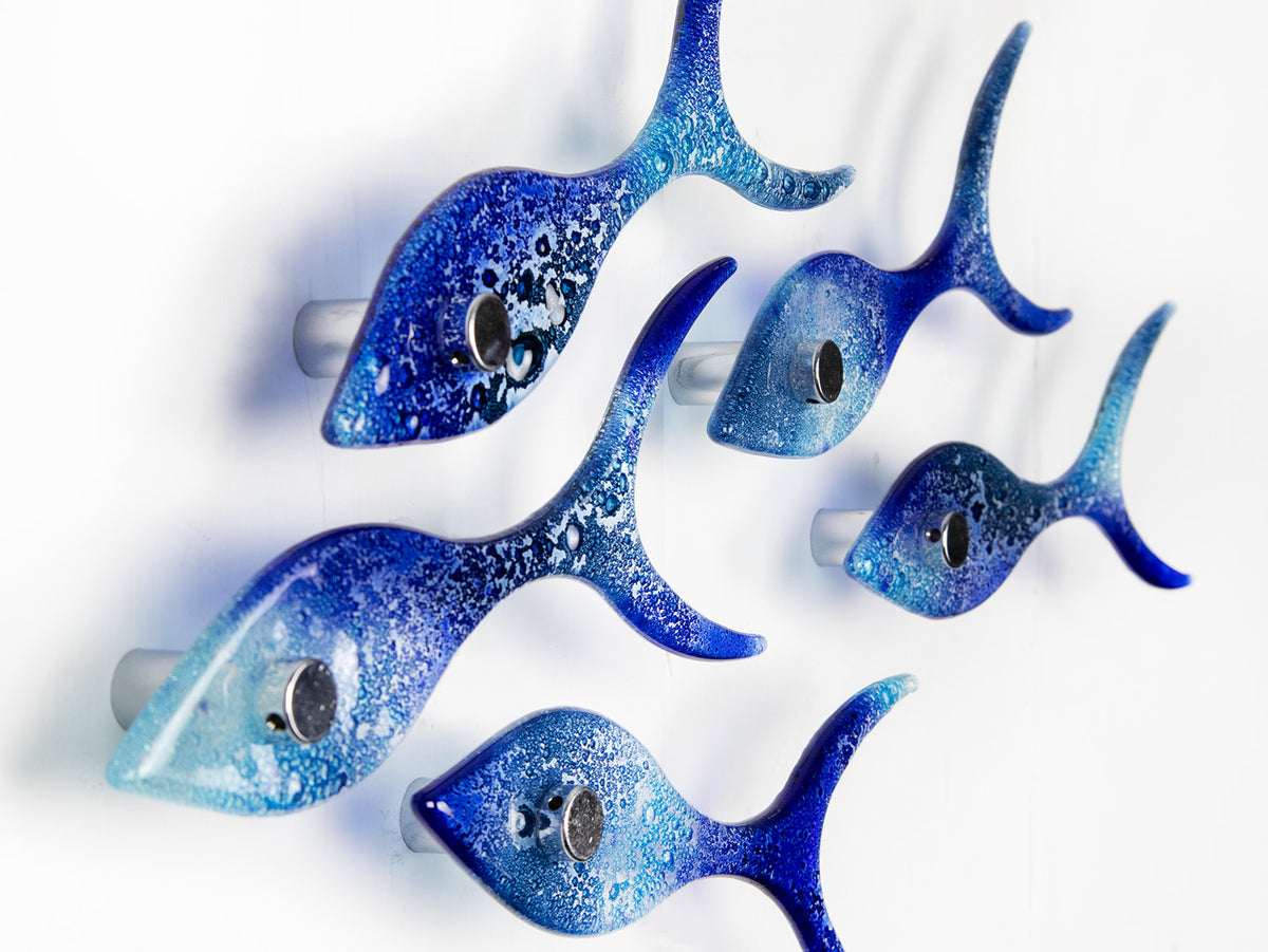 Side image of five fused glass fish in a shoal shape in coastal blues. Handmade ocean inspired wall art.