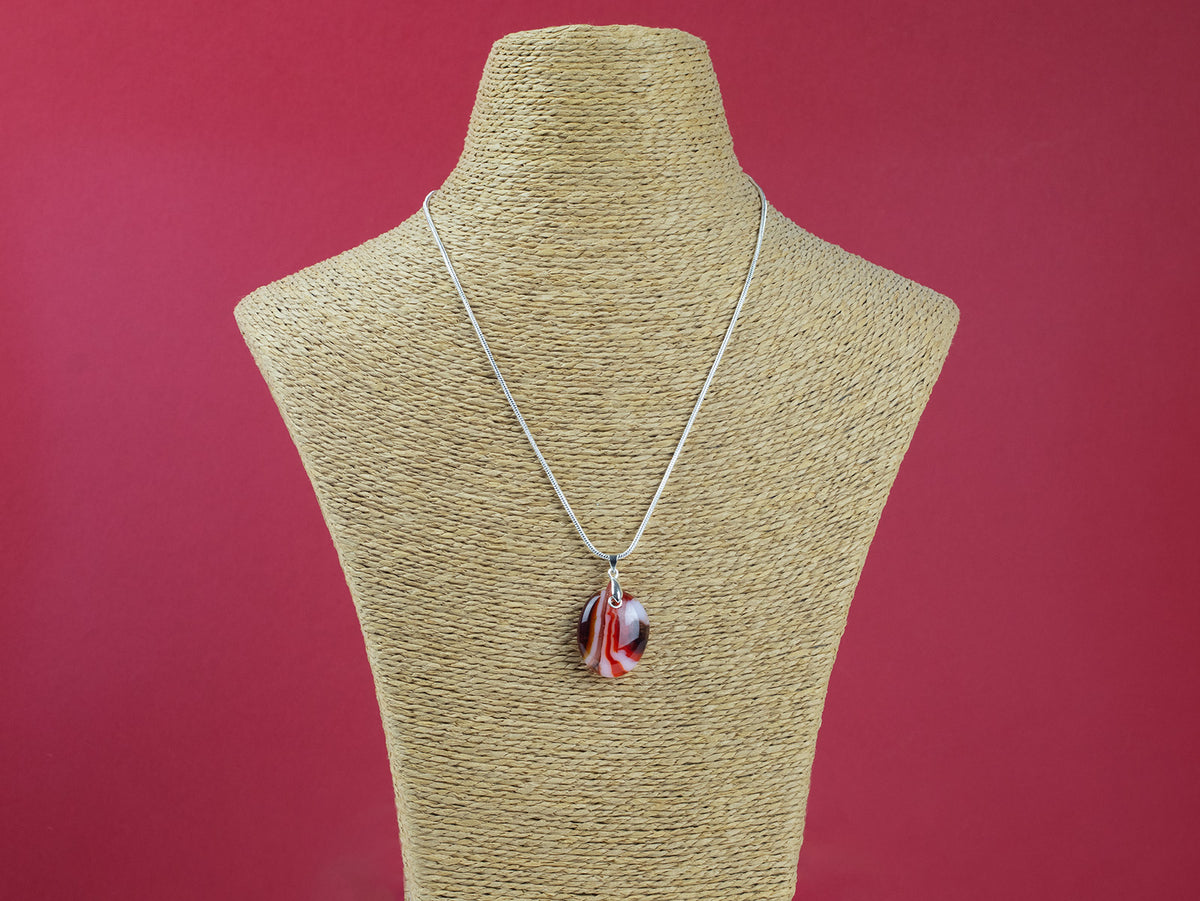 A sterling silver chain necklace with a round fused glass pendant featuring an autumnal, red design, handmade in vibrant colours and seen on a mannequin