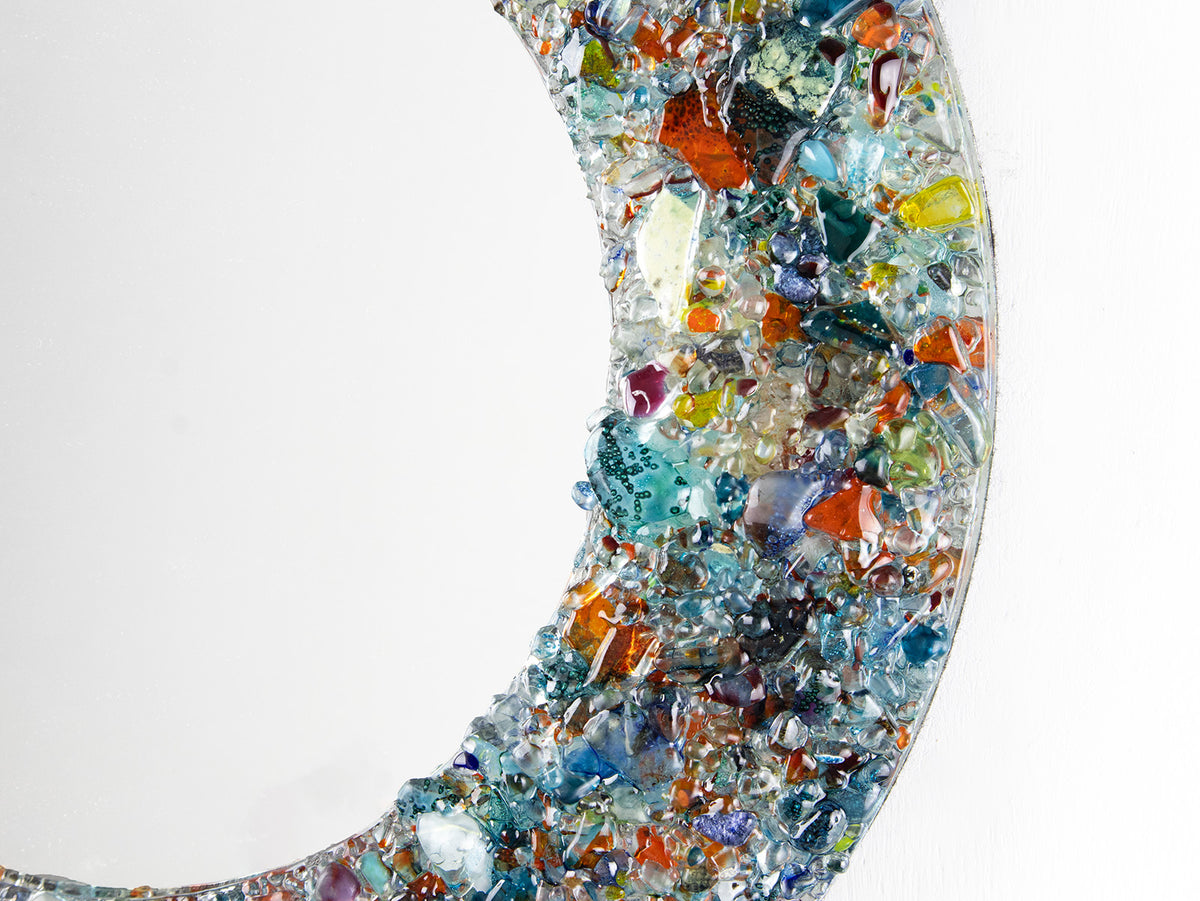 A close up of a fused glass round mirror handmade using multi coloured recycled glass, creating a striking piece of wall art. 
