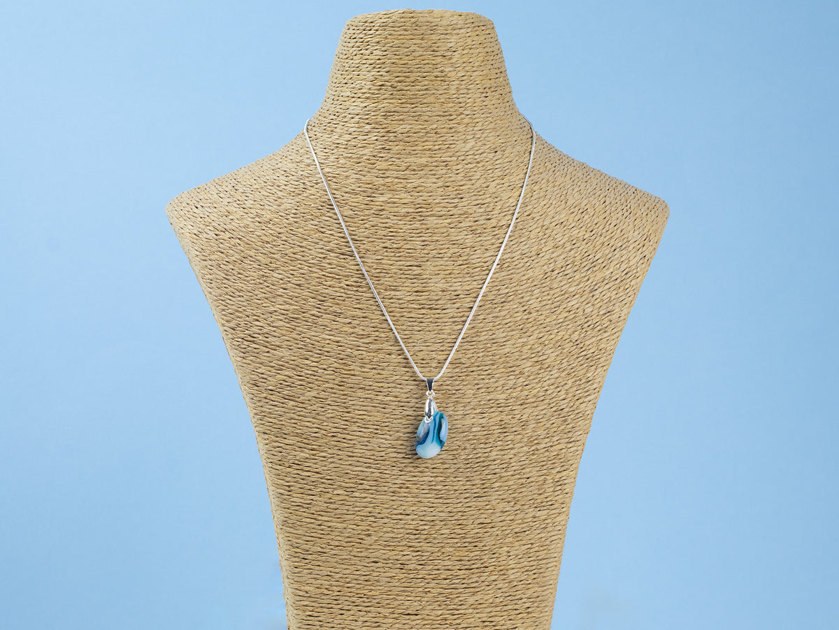 A sterling silver chain necklace with a teardrop-shaped fused glass pendant handmade featuring a ocean blue marbled design seen on a mannequin. 