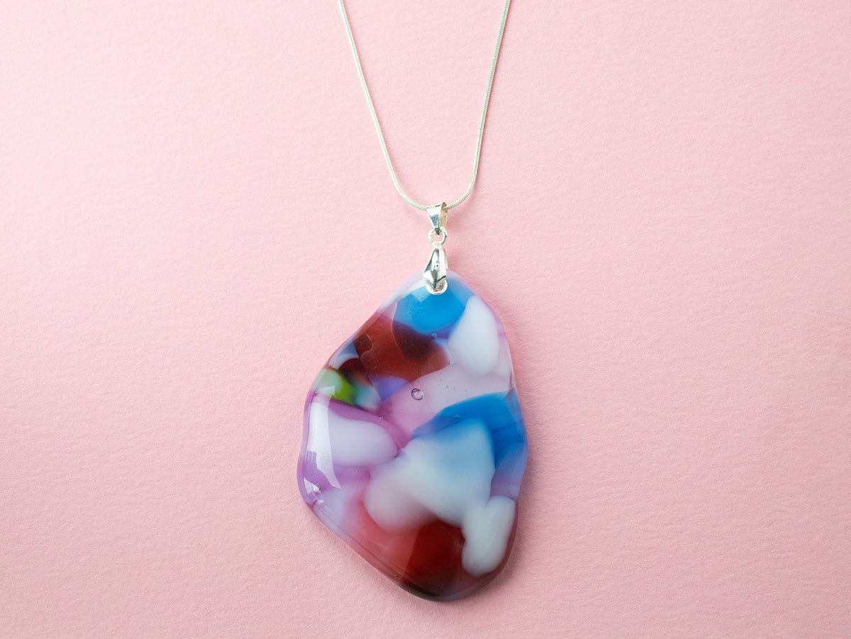 A sterling silver chain necklace with a fused glass pendant featuring a marbled pattern of soft pinks and delicate blue and red hues.