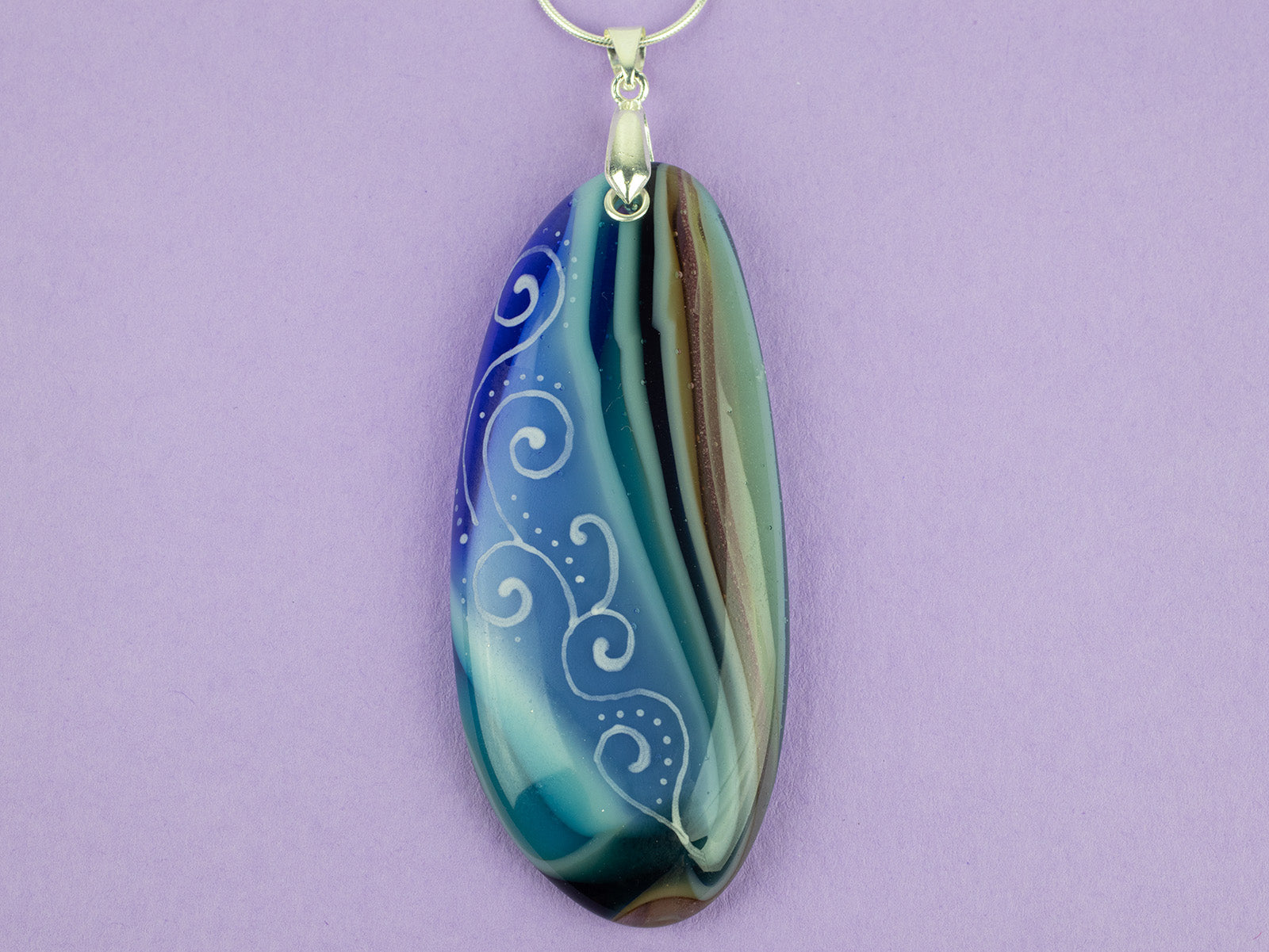 Close up of fused glass pendant necklace, handmade in coastal hue, with an organic, swirling hand-painted design. 