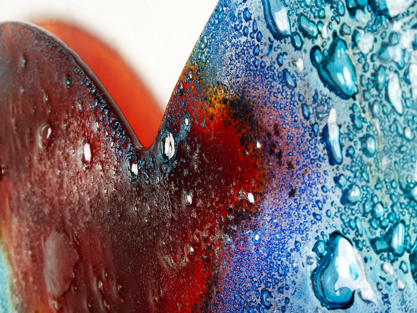 A detailed close up of this striking 95cm fused glass hear shaped wall panel handcrafted in Cornish studio in bright reds, aqua blues and lots of textured detailing. 