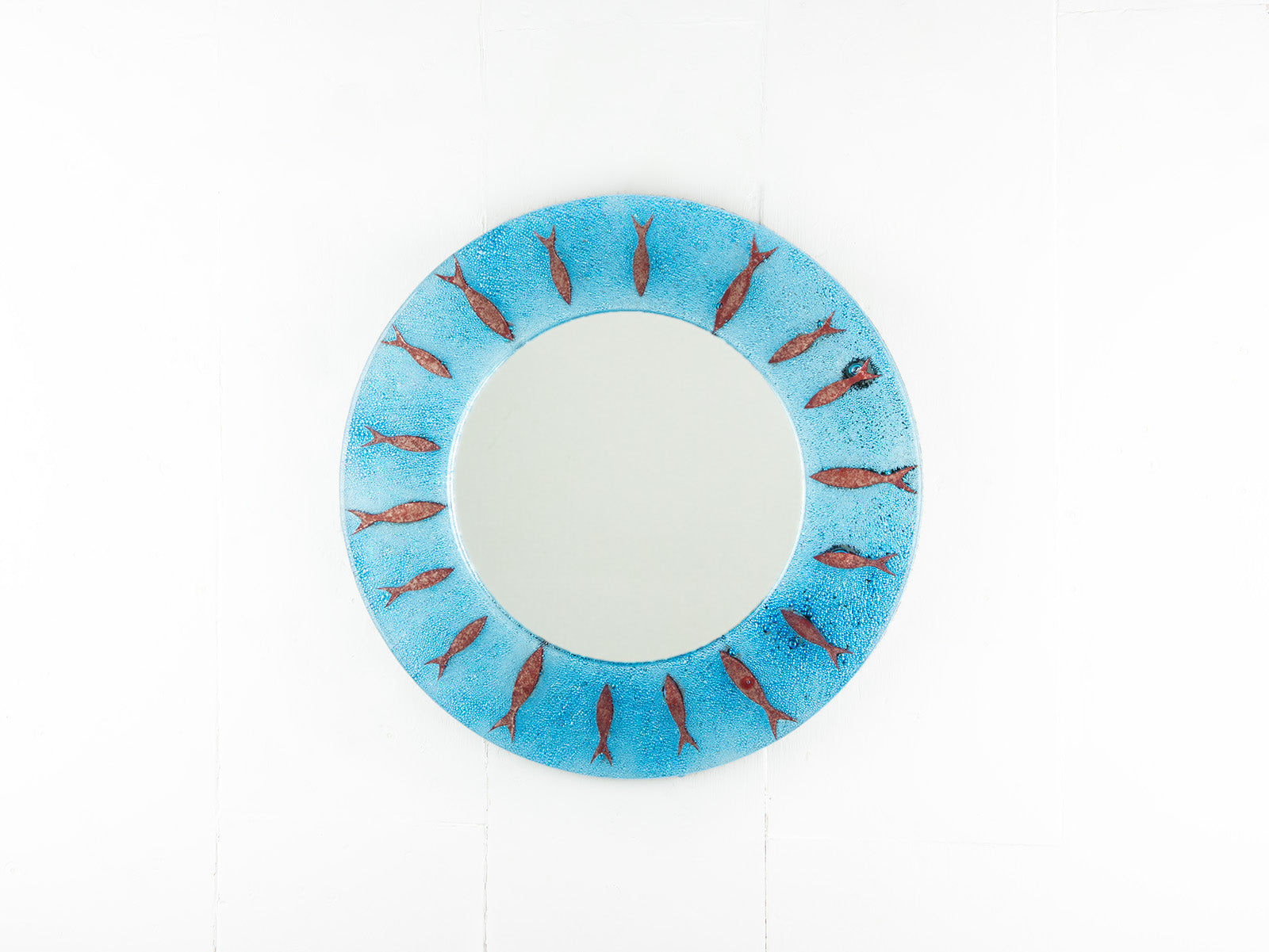 Circular fused glass mirror, featuring circular design of copper fish with an aqua blue colour-way, creating a coastal and ocean inspired wall art design. 