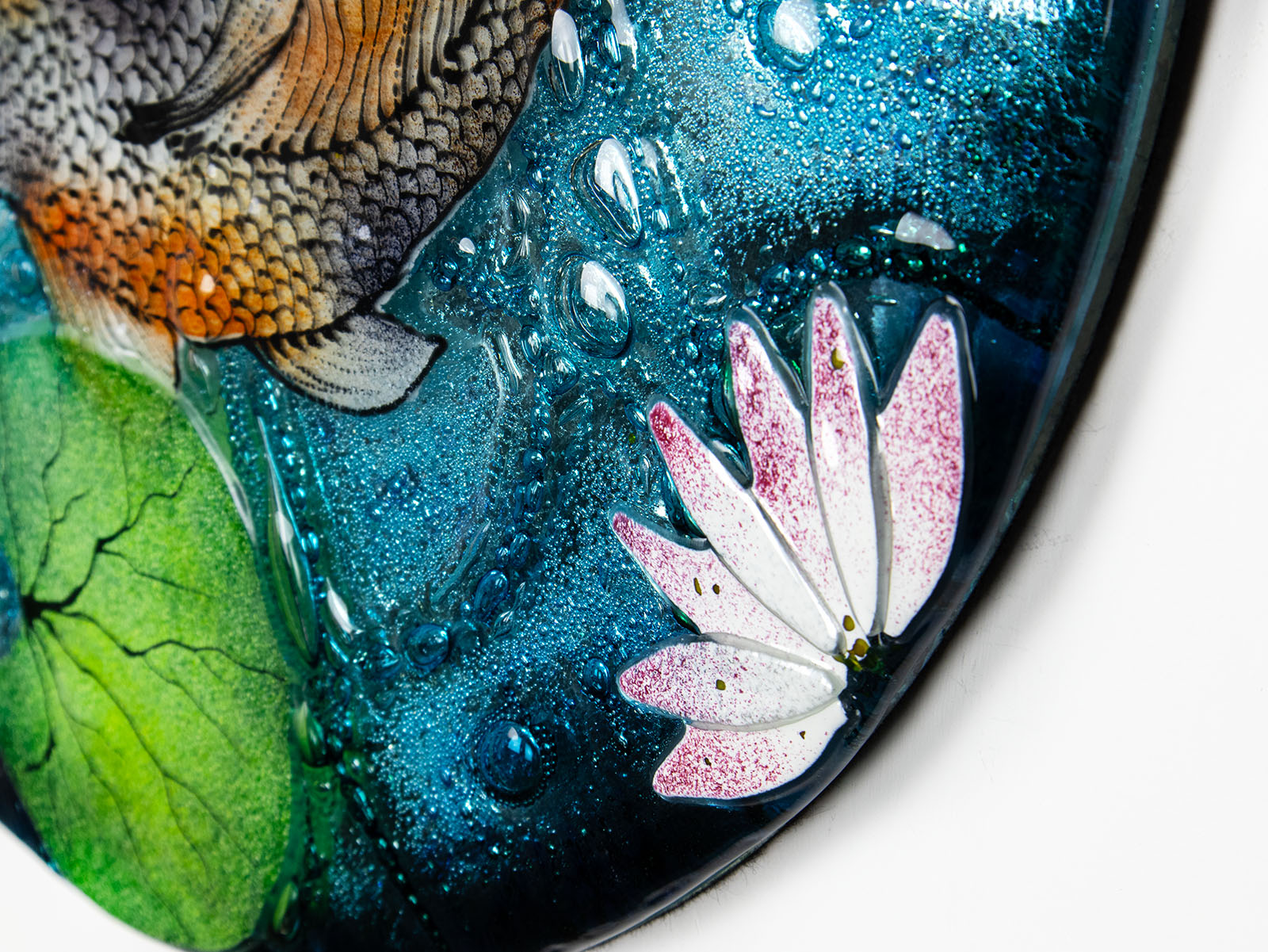 A close up of a lily in a fused glass round panel featuring hand-painted koi carp design with waterlilies and marine blue background. 