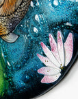 A close up of a lily in a fused glass round panel featuring hand-painted koi carp design with waterlilies and marine blue background. 