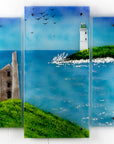 A fused glass triptych in coastal colours, with distant soaring sea birds, a lighthouse sat on a cliff and a Cornish tin mine. Hand-made coastal wall art, with texture. 