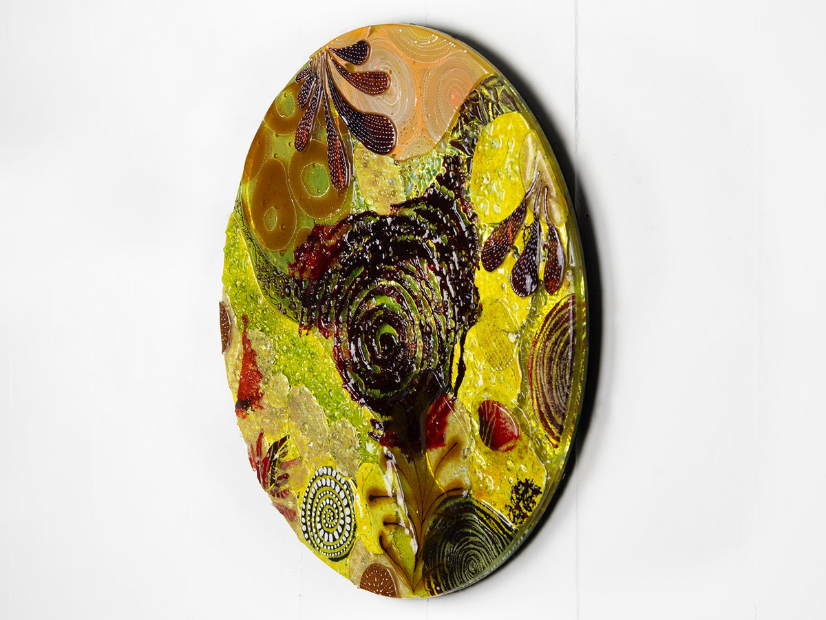 A fused glass round panel featuring organic autumn inspired patterns and shapes, in a vibrant yellow colour-way, handmade and inspired by the autumnal season. 