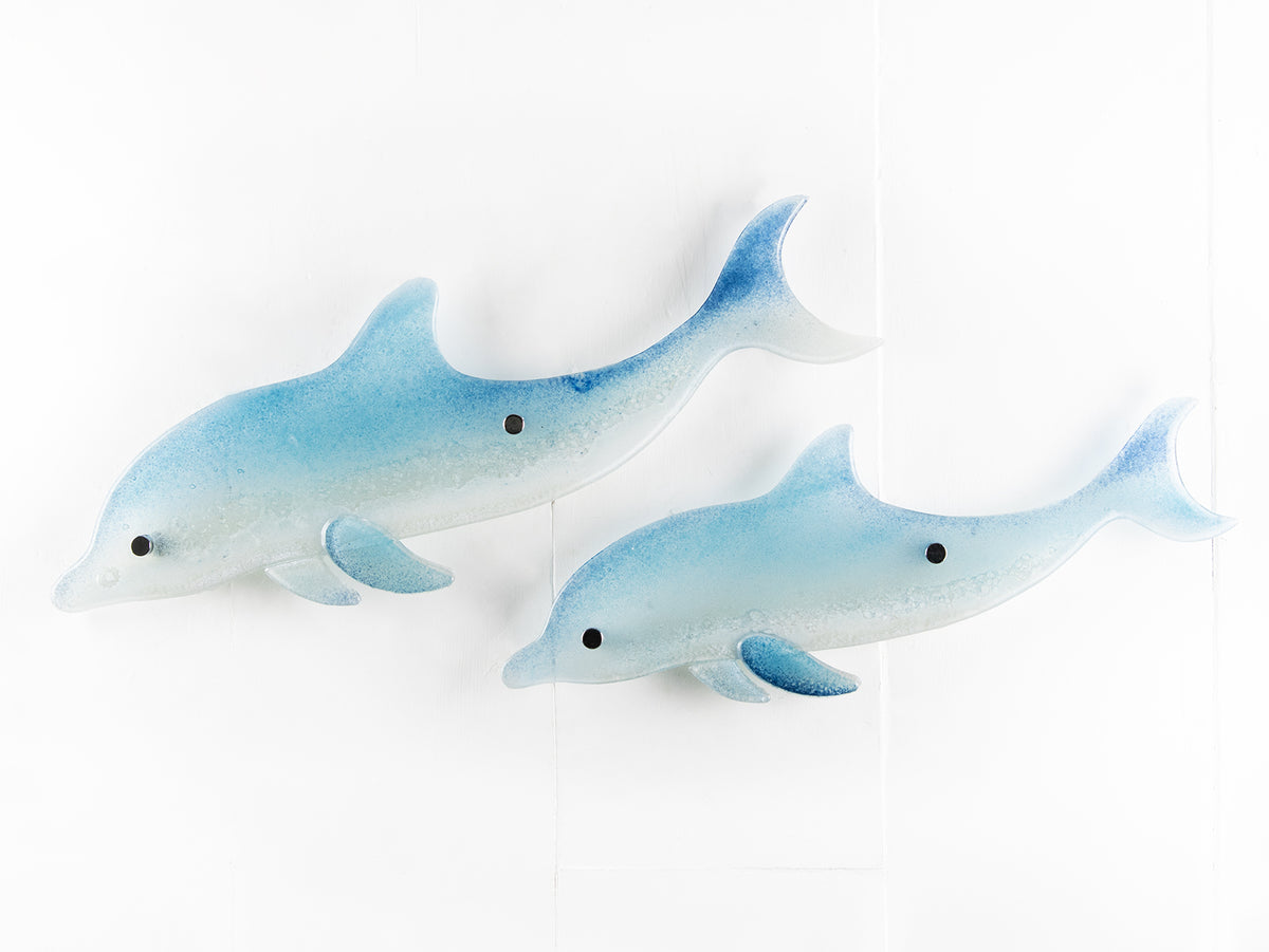 Two blue dolphin wall art panels, handmade i fused glass, designed in soft coastal blues and whites. 