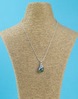 A sterling silver chain necklace with a teardrop-shaped fused glass pendant handmade featuring a ocean blues and sea greens in a marbled design seen on a mannequin. 