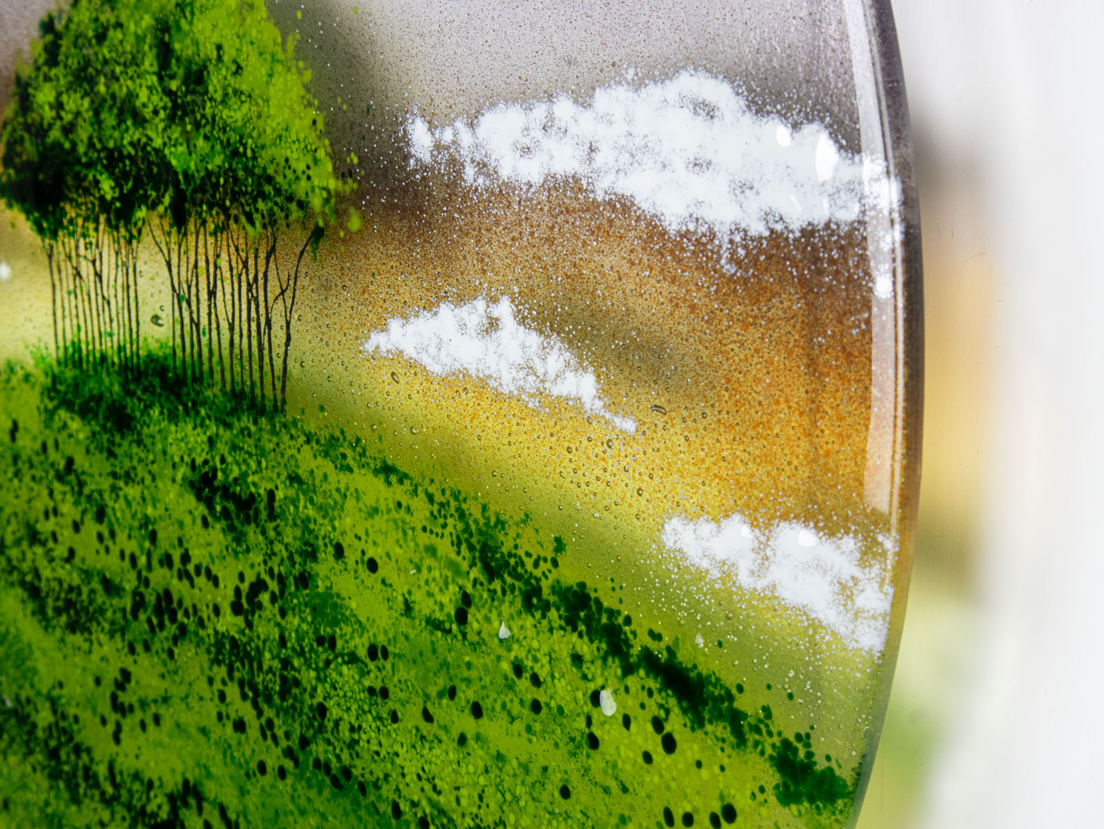 A close up of fluffy white clouds on a fused glass round panel featuring a design of the "Nearly Home Trees" located on a hill over-looking the A30. 