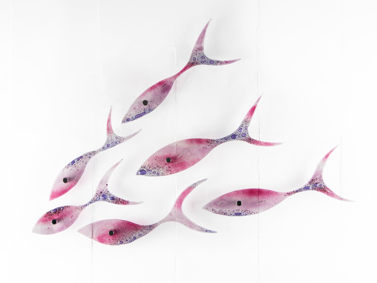 A fused glass shoal of fish, with individual fish installed in a bright pink and bubbled purple colour-way. 
