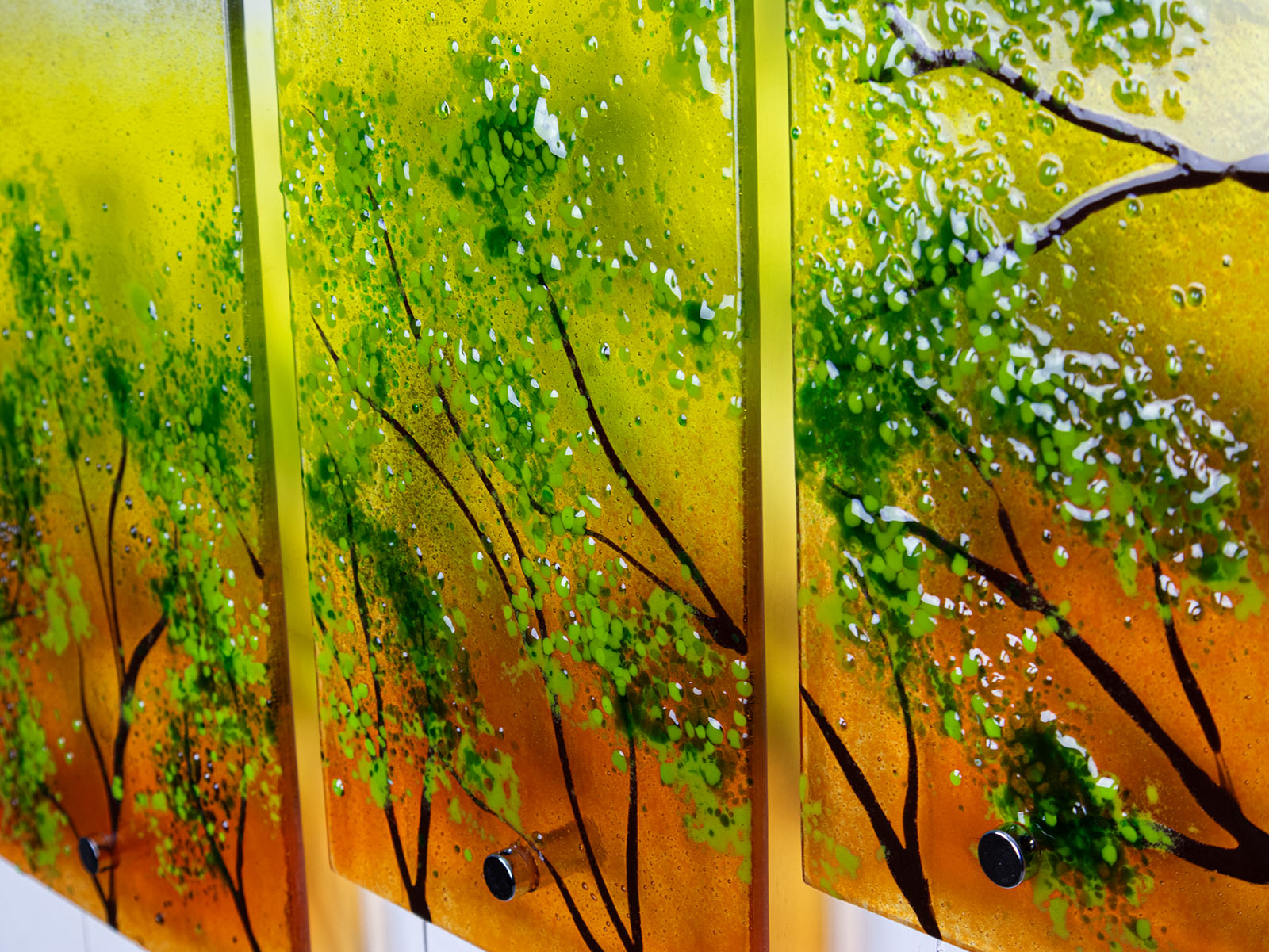Close up of fused glass quintych featuring an abstract design of a woodland, with a vibrant sunset sky and textured detailing. 