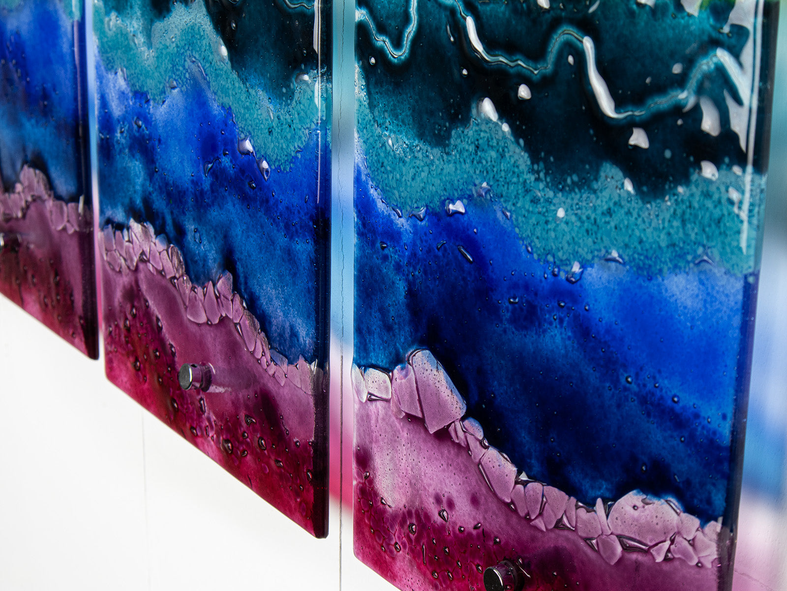 Abstract wall art made of multiple vertical panels with layered fluid design in deep blue, teal, purple, and magenta, photographed close up against a white background.