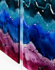 Abstract wall art made of multiple vertical panels with layered fluid design in deep blue, teal, purple, and magenta, photographed close up against a white background.