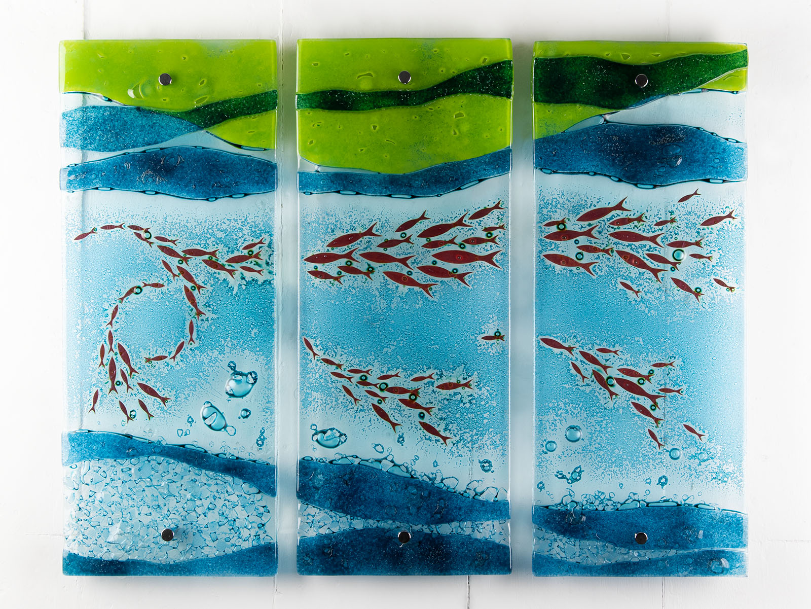 A fused glass triptych featuring marine blues and greens in an ocean design, with copper fish and textured detail. 